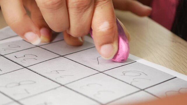 A hand uses an eraser on a paper at a wooden table