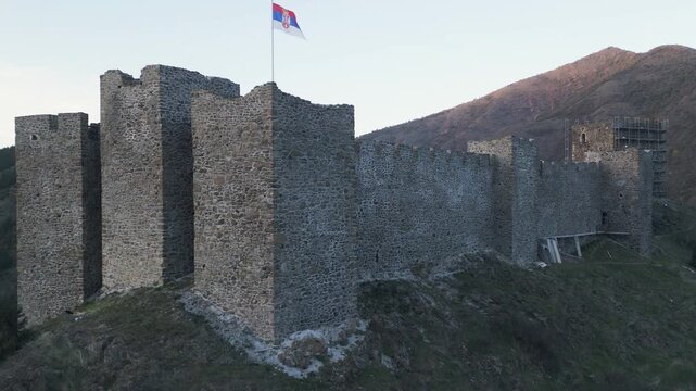 Drone reveal of Maglic fortress walls and waving Serbian flag at dusk, western Serbia.