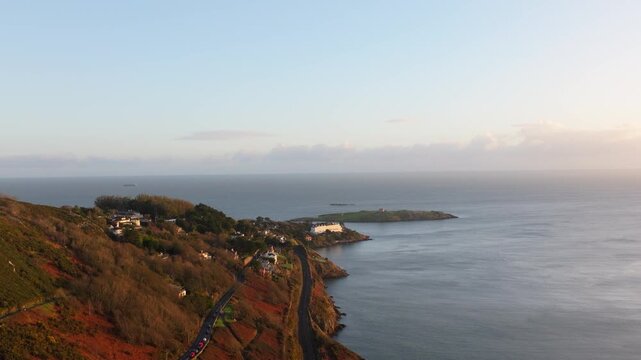 A scenic coastal road lined with homes overlooks Dalkey Island and the expansive ocean. The soft morning light creates a tranquil atmosphere, ideal for travel and nature projects.