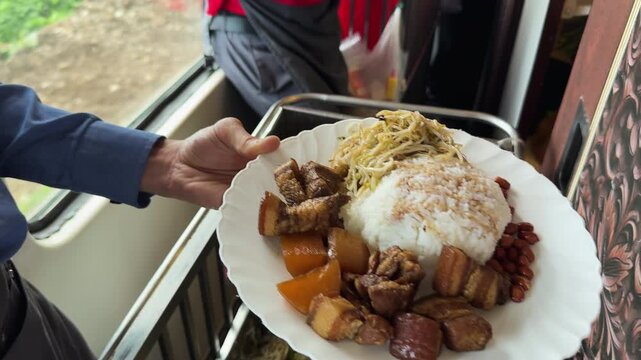 Train meal served by onboard staff beside a window on the Hanoi to Hoi An route, featuring rice, noodles, braised pork, and beans in a candid travel-food moment.