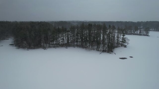 Drone flight ascending and tilting down the camera during a winter storm in a frozen lake with islands, freezing temperatures, Harold State Forest Park, Massachusetts