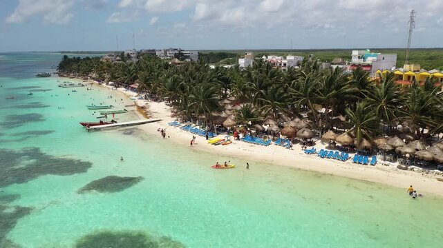 Stunning aerial view of Bacalar, Mexico featuring crystal clear turquoise lagoon waters, palm-lined beach, and thatched huts. Tropical paradise scene with people enjoying the Caribbean coastline.