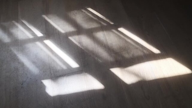 Abstract view of sunlight casting geometric window shadows across a wooden floor in a quiet interior setting.