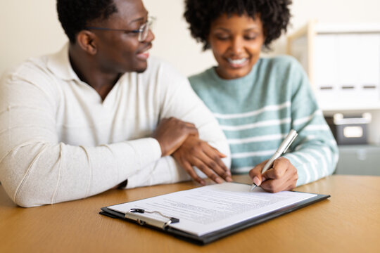 Couple smiling and signing contract or agreement at office desk. selective focus on hands.