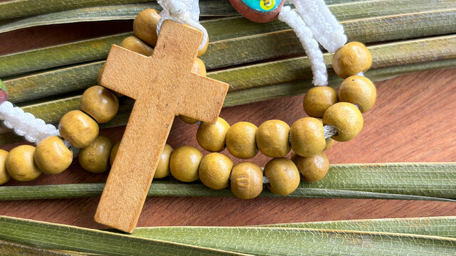 Wooden Holy Rosary laid on striped blessed pam leaf.