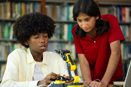 Indian and african american students through hands-on robotic arm engineering project. Students focus intently, collaborating at shared workbench. Bright room, large windows. Education, Back to school