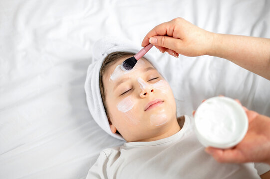 Woman applying skincare mask to child face during home beauty routine