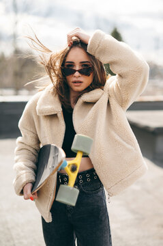 Stylish hipster woman standing on roof with skateboard in hands