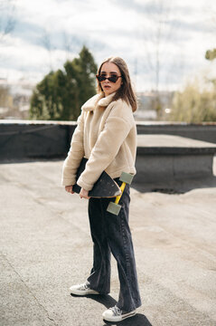 Stylish woman holding skateboard while standing on roof