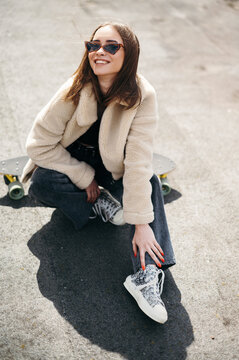 Woman sitting on skateboard and smiling on camera outdoors