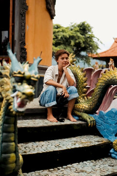 Woman with camera sitting between dragon statues at monastery, Bali