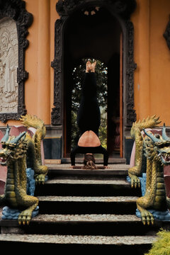 Woman yogi in headstand between ornate dragon sculptures at temple