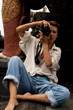 Woman photographer sitting on temple floor shooting with camera, Bali
