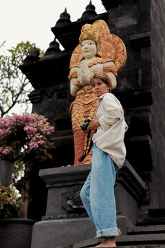 Woman photographer on temple steps before golden deity statue, Bali