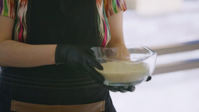 Young female chef in khan atlas holding glass bowl of rice for pilaf