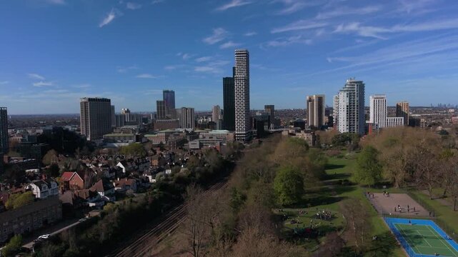 Croydon skyline aerial view above railway tracks with trains passing. Urban area with modern skyscrapers. Still aerial and flying towards the city center. Public transport in motion on a sunny day.