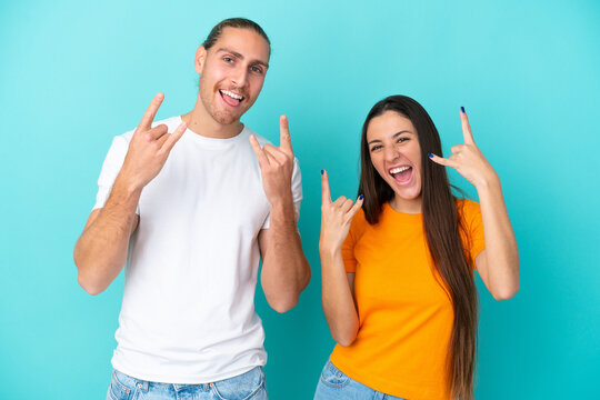 Young caucasian couple isolated on blue background making rock gesture