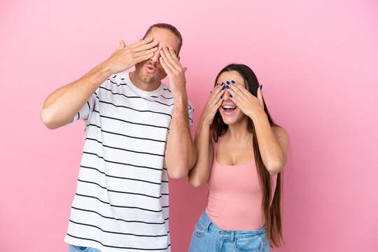 Young caucasian couple isolated on pink background covering eyes by hands