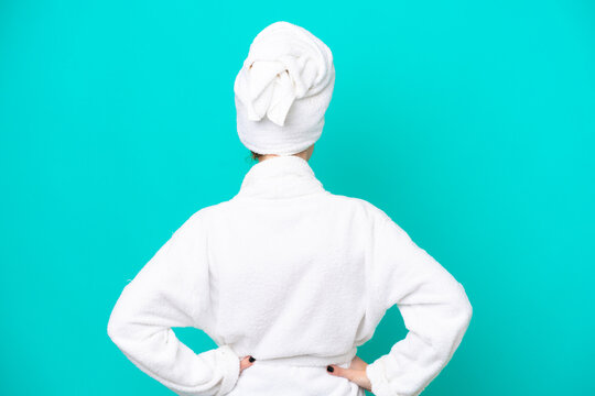Young woman in a bathrobe isolated on blue background in back position