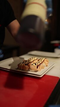 Vertical screen chef pouring sauce over sushi close up slow motion rich texture glossy topping japanese cuisine food detail