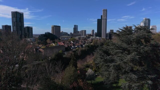 Croydon skyline aerial view from Park Hill above the trees. Aerial rising view from public park with modern skyscrapers in city center. Peaceful environment on a sunny day with blue sky in springtime.