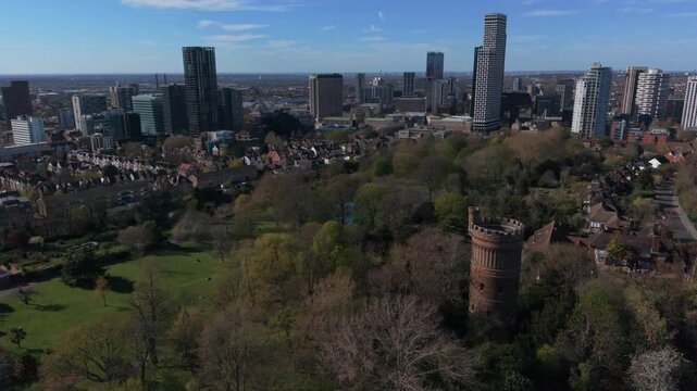 Croydon skyline on a sunny day. Aerial view from Park Hill with historic water tower. Forward motion above green park with historic landmark towards tall modern skyscrapers in city center.