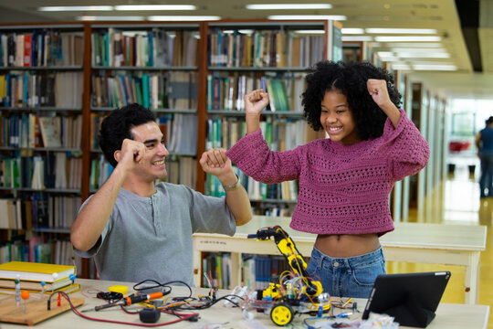 Young teacher guides students through hands-on robotic arm engineering project. Students focus intently, collaborating at shared workbench. Bright room, large windows. Education, Back to school