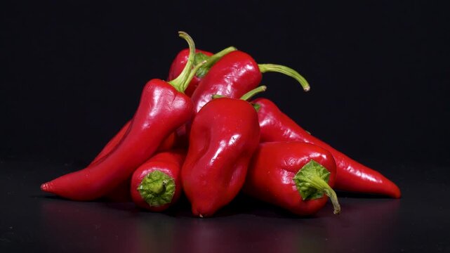 Close-up footage of red capia peppers with green stems on black background.