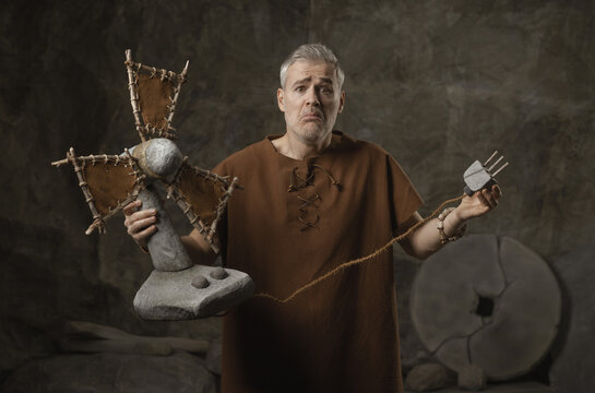 Confused Caveman Holding Stone Fan and Plug in Prehistoric Cave