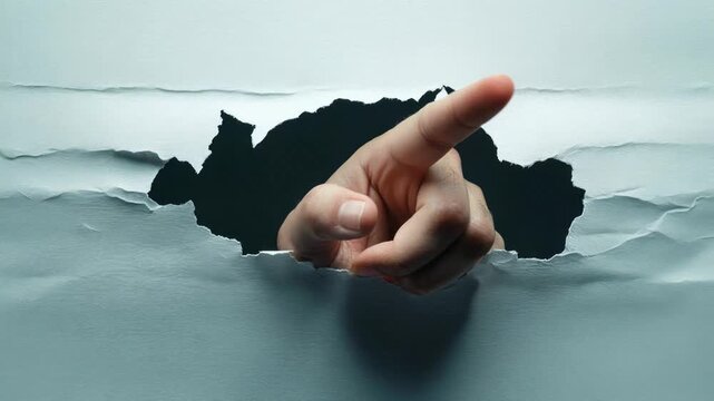 Male hand with pointing finger breaking through a hole in a piece of paper and gesturing forward