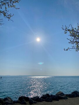 Bright sun shining over sparkling blue lake with rocky shore under clear sky.