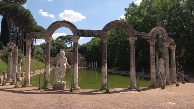 The Canopus pool at Villa Adriana, Tivoli, Italy. Ancient Roman columns, arches, and marble statues reflect imperial grandeur under a sunny sky.