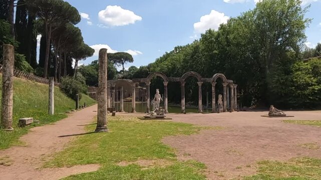 Scenic view of Villa Adriana Canopus pool area with ancient Roman columns, marble statues, and lush greenery in Tivoli near Rome, Italy. UNESCO World Heritage Site.