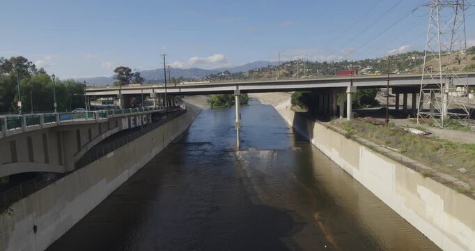 Cinematic daytime 4K 10-bit footage captured along the Los Angeles River showing flowing water channels running beneath a bridge near the Golden State 5 Freeway.