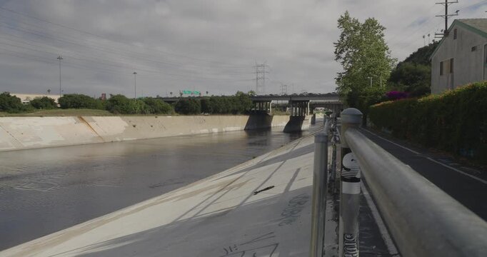 Cinematic daytime 4K 10-bit footage captured from the Los Angeles River walking path facing the busy 5 and 110 freeway interchange. The shot showcases dense vehicle traffic, and layered overpasses.
