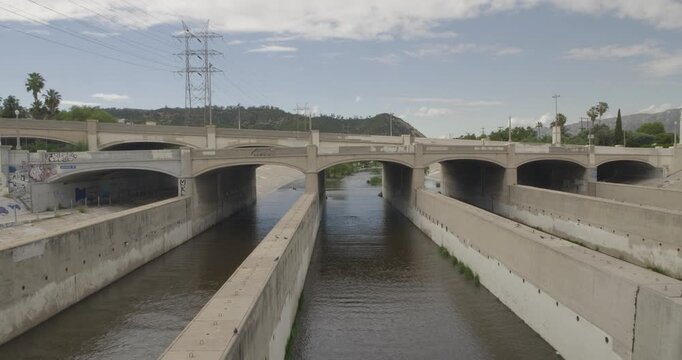 Cinematic daytime 4K 10-bit footage capturing an aqueduct bridge structure spanning the Los Angeles River corridor. The shot highlights the industrial geometry of the crossing, the surrounding river.