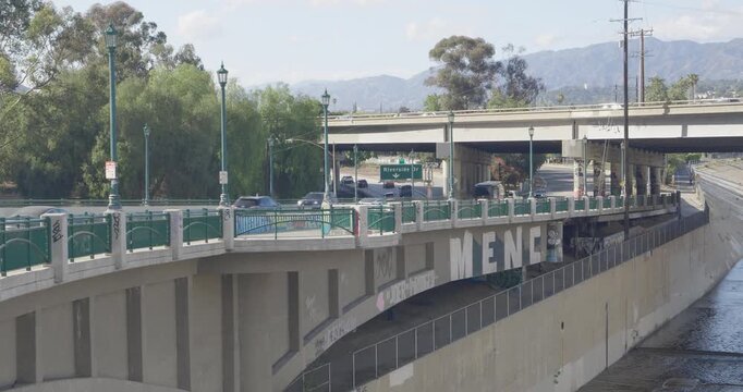Cinematic daytime 4K 10-bit footage captured along the Los Angeles River showing vehicles driving across a bridge running parallel to the concrete water channels below.