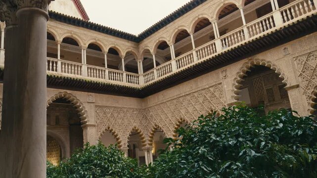 Beautiful lush courtyard garden inside Real Alcazar in Seville, Spain, featuring intricate Moorish arches, detailed walls, and vibrant greenery in a historic palace setting.