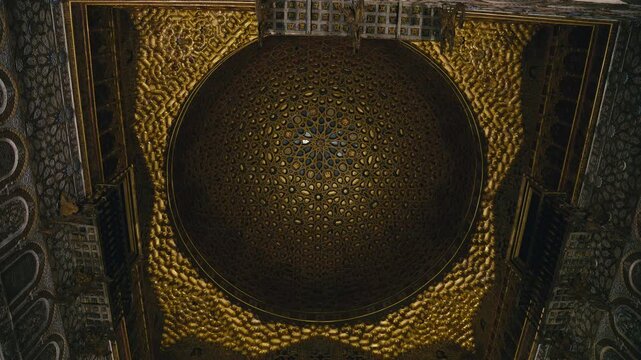 Intricate Moorish ceiling inside Real Alcazar in Seville, Spain, featuring geometric patterns, golden ornamentation, and symmetrical Islamic design in a historic architectural setting.