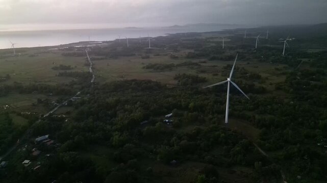 Aerial view of wind turbines stand tall over lush greenery and coastal views on Guimaras Island. Ideal for renewable energy projects or environmental documentaries.