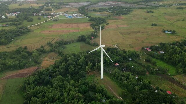 Aerial drone shot of wind turbine amidst green fields and rural homes on Guimaras Island, Philippines. Great for environmental projects or energy-themed content.