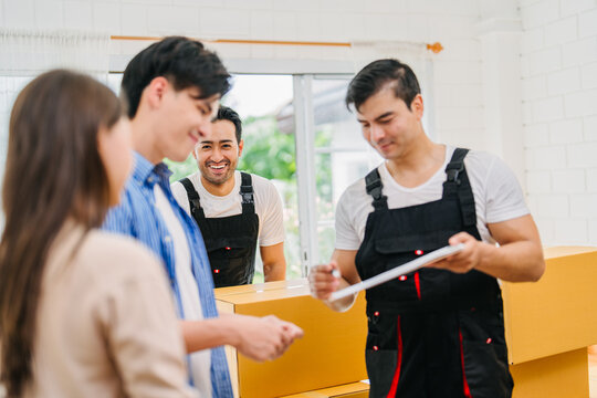 Young couple checking documents with professional movers during new home relocation. Delivering boxes, unpacking, happy domestic life apartment. Real estate, move service, logistic, household business