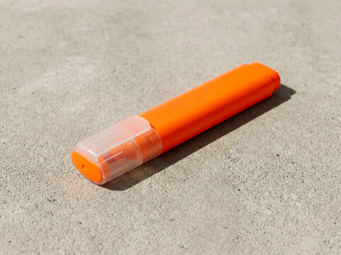 Bright orange permanent marker with a transparent cap lying on a textured concrete surface