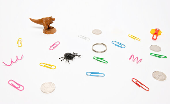 Random collection of small objects on white background, paper clips, coins, toy spider and dinosaur, chaos and variety concept