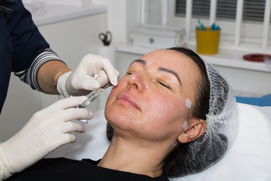 A cosmetologist performs lip augmentation injections on a middle-aged woman.