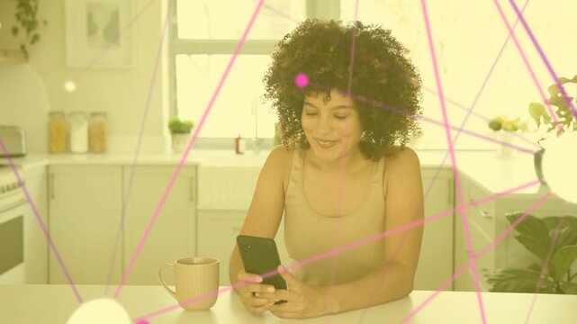Mid-adult woman tapping smartphone in kitchen, animating pink-purple overlays and smiling for ads