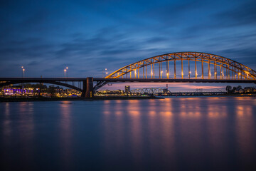 Fototapeta premium Nijmegen, a town in the Netherlands situated on a river in the evening at the blue hour, with the all the lights on. 