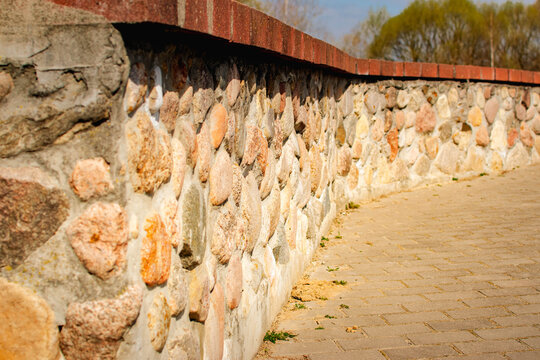 decorative natural stone retaining wall with brick top edge and paved walkway in landscaped park setting