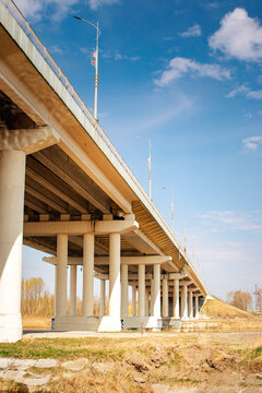 low angle view of massive concrete highway bridge with repeating pillars and dramatic perspective under blue sky