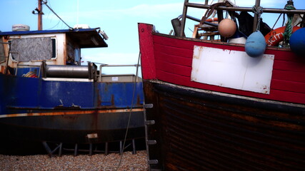 Fishing boats rest on the shore near a dock at low tide with colorful buoys and a clear sky in the background © Neil